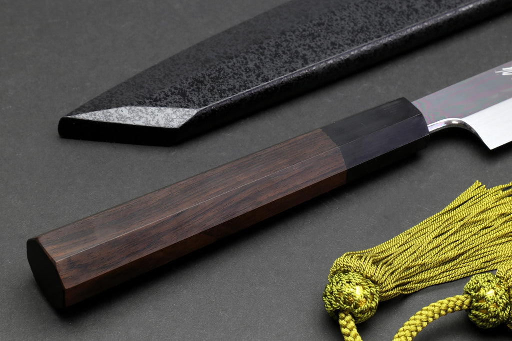 Japanese knife with dark rectangular handle and mirror blade, plus green tassel cord in frame.