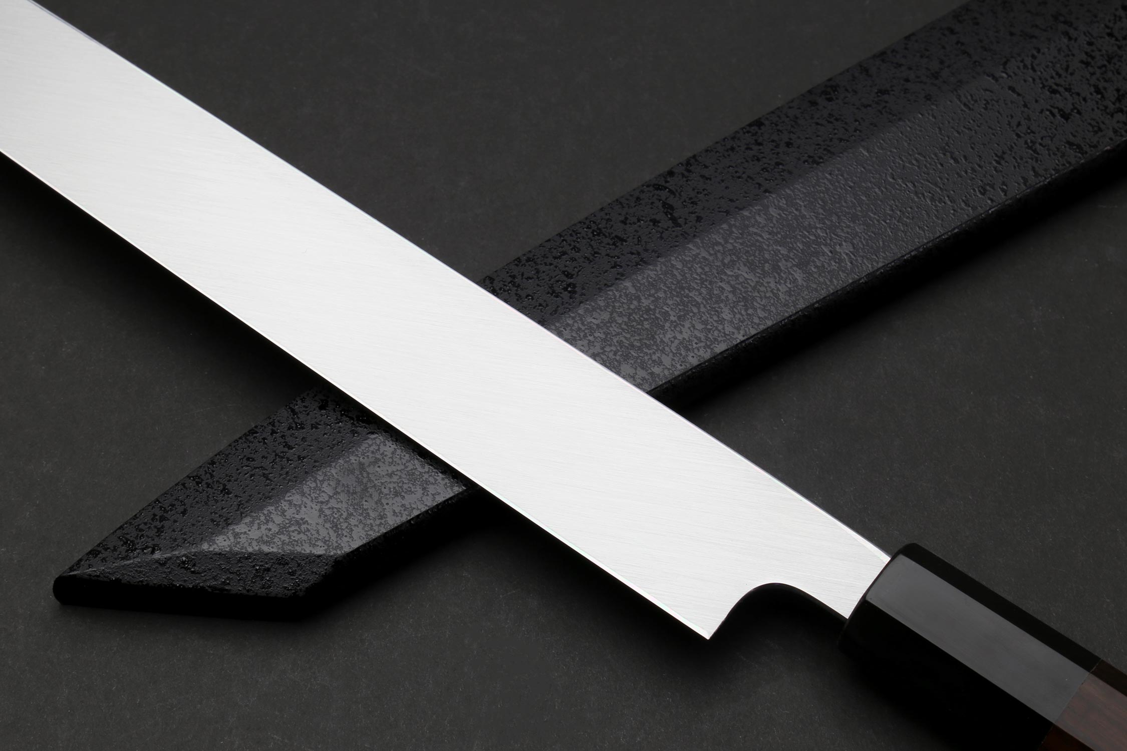 Japanese knife with silver mirrored blade and dark handle, angled view showing edge and curve.
