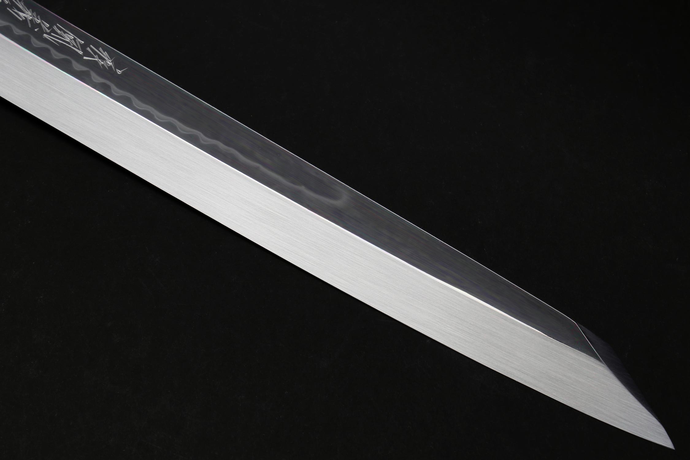 Japanese knife blade close-up with mirror finish and faint etched pattern along the back edge.
