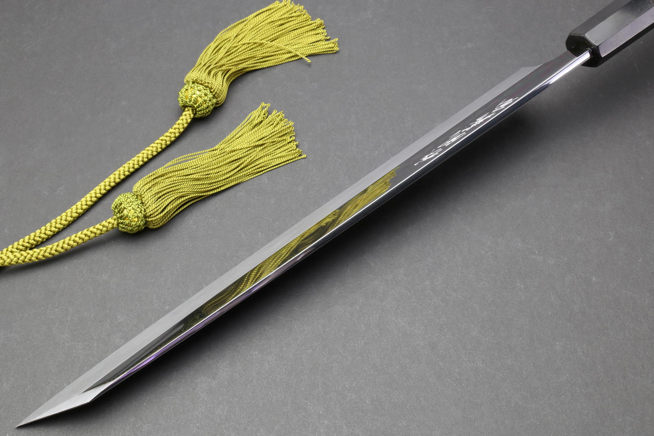 Japanese knife with silver blade and dark handle, with green cord and small tassels nearby.