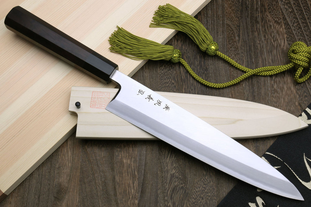 Japanese fish filet knife with ebony handle and silver blade, side angle on wood