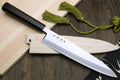 Japanese fish filet knife with ebony handle and silver blade, side angle on wood