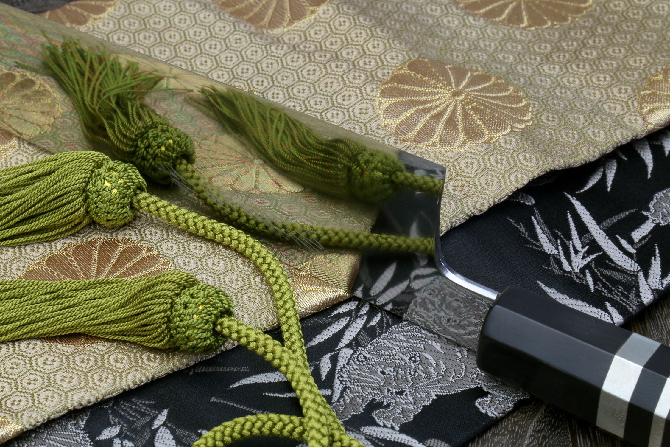 Gyuto chef knife close-up with mirror blade and ebony handle, shown with green cords