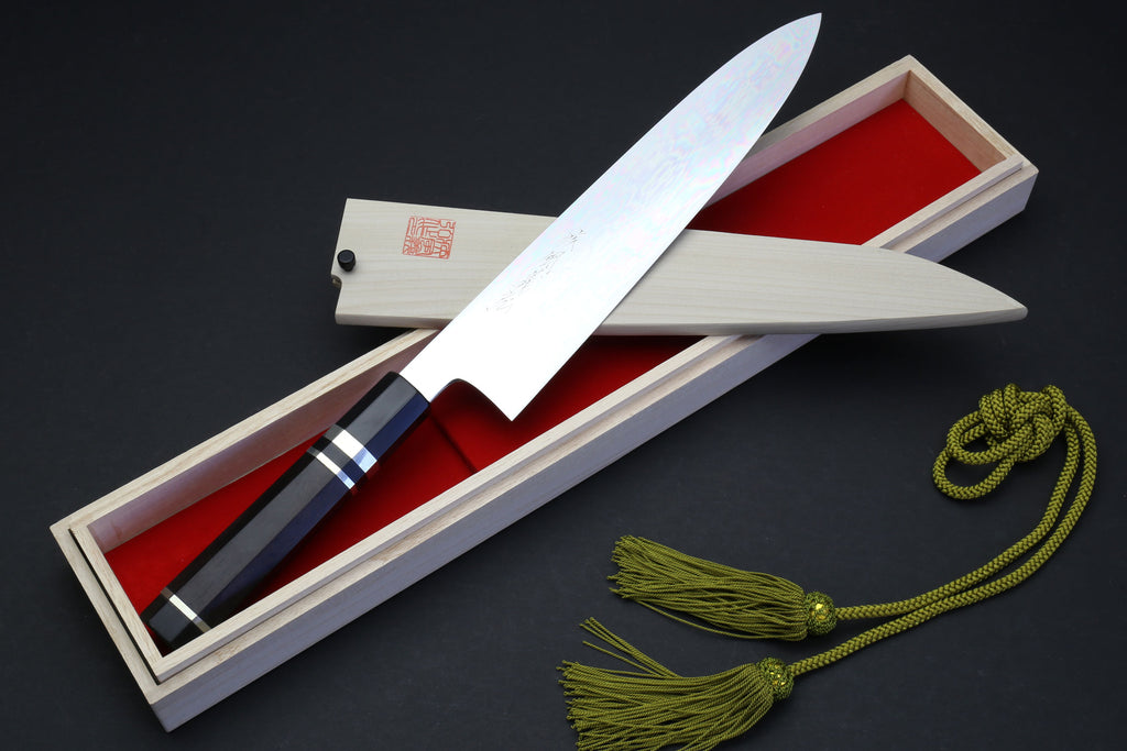 Chef knife in box: mirror-polished blade, ebony handle, green cord tassel.