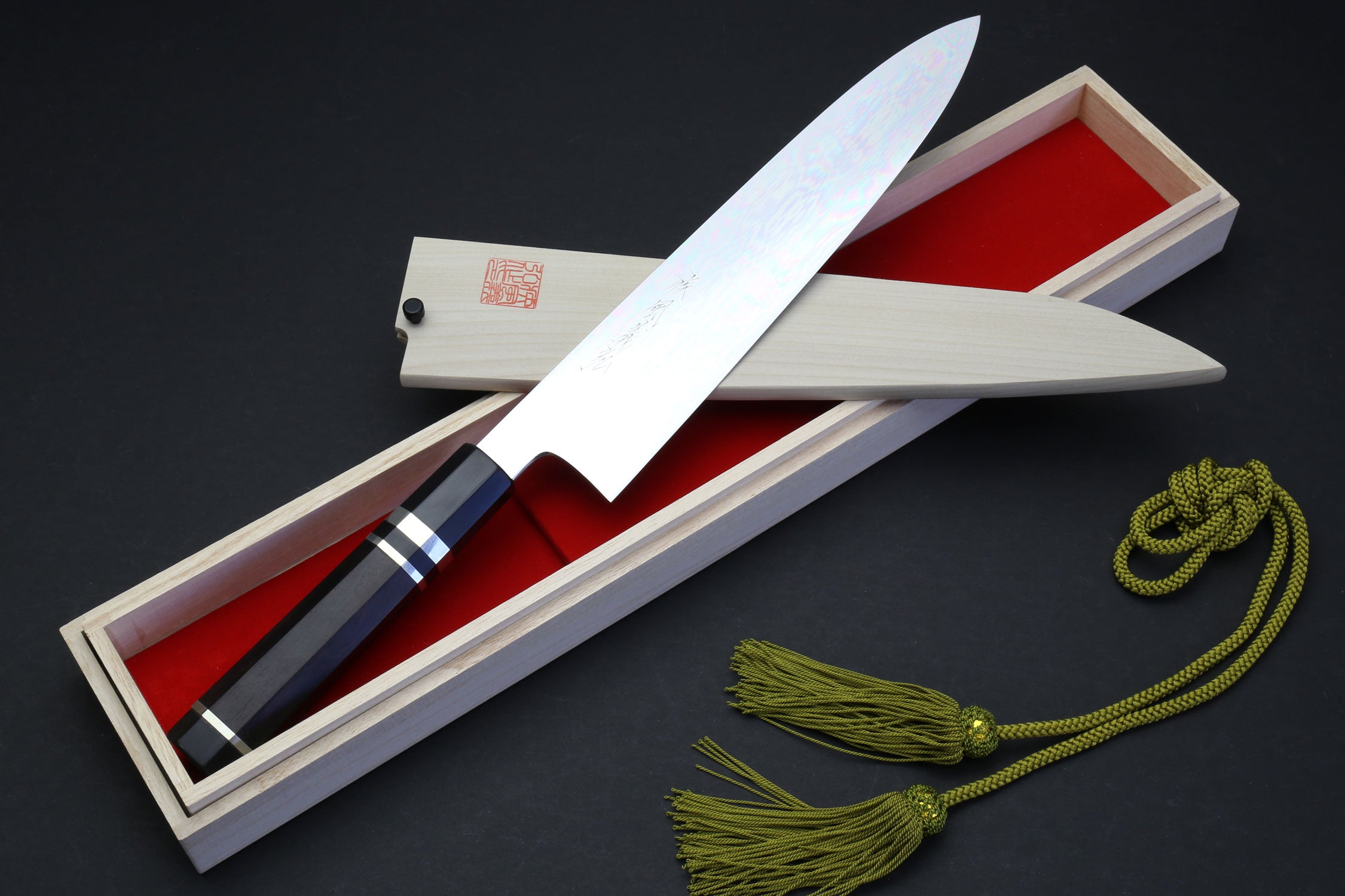 Chef knife in box: mirror-polished blade, ebony handle, green cord tassel.