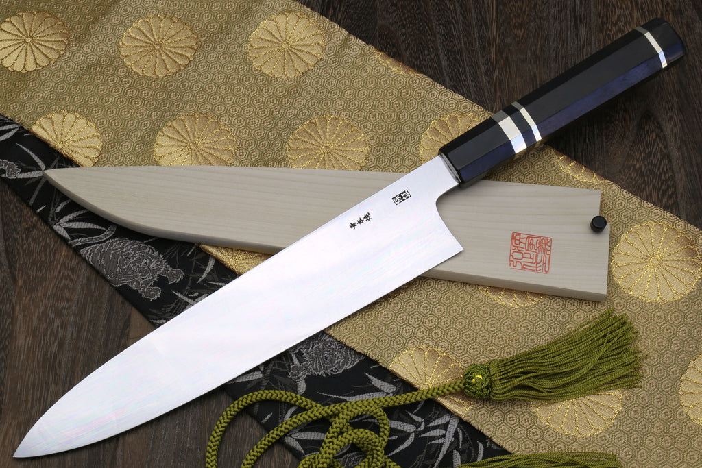 Gyuto chef knife with mirror-polished blade and ebony handle, lying on patterned cloth
