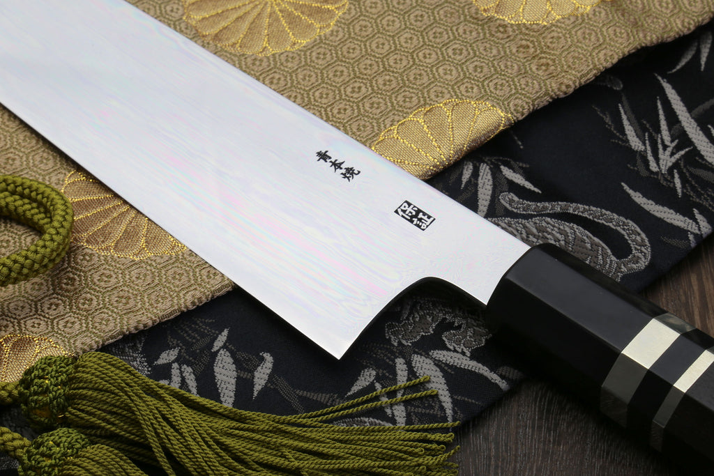 Gyuto chef knife blade close-up with mirror sheen and small stamp near heel