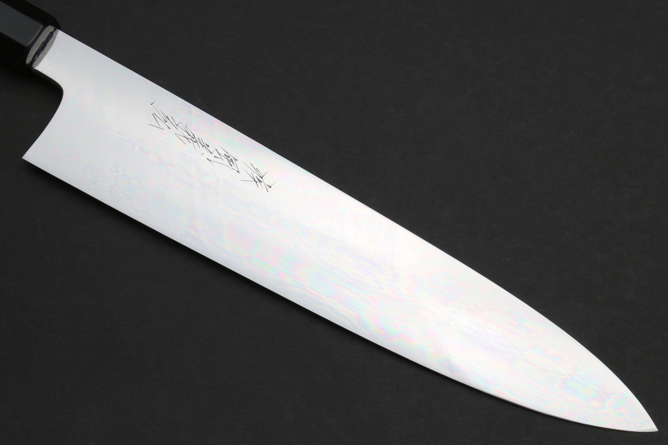 Gyuto chef knife blade close-up with mirror-polished finish and faint engraving