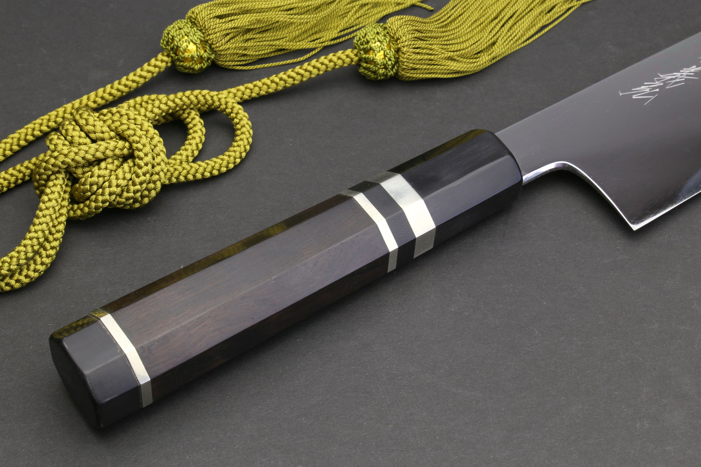 Gyuto chef knife handle close-up with striped accents, shown with green cord