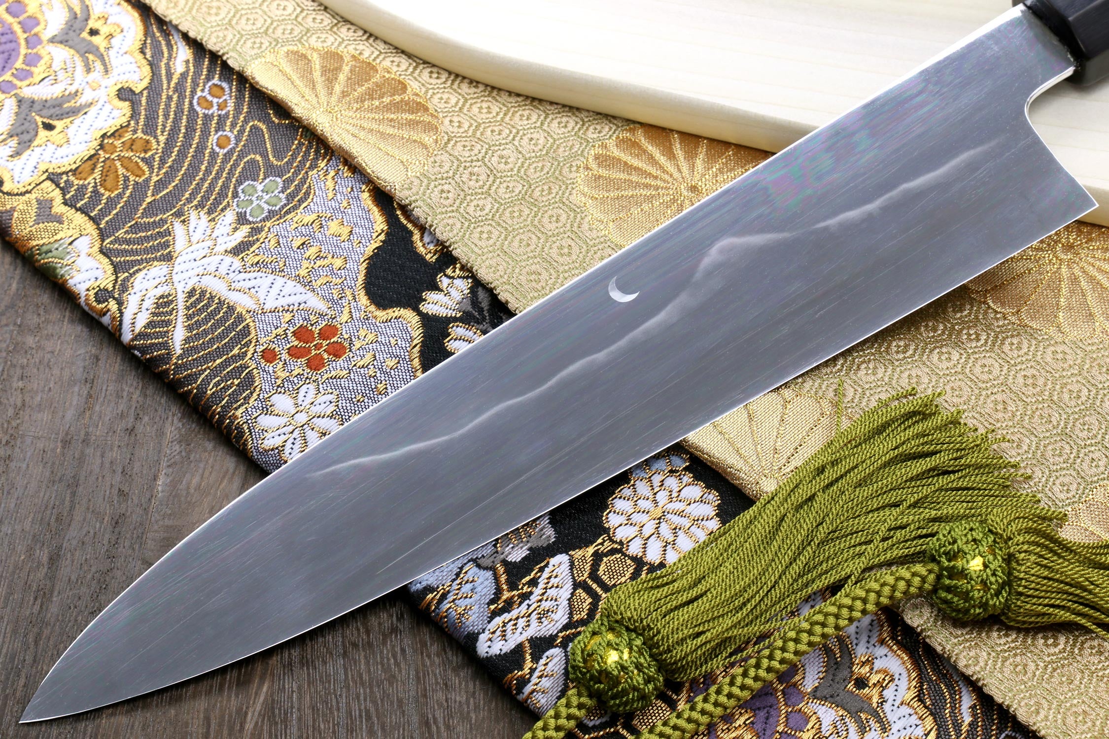 Gyuto chef knife with dark blade edge and green cord on patterned fabric
