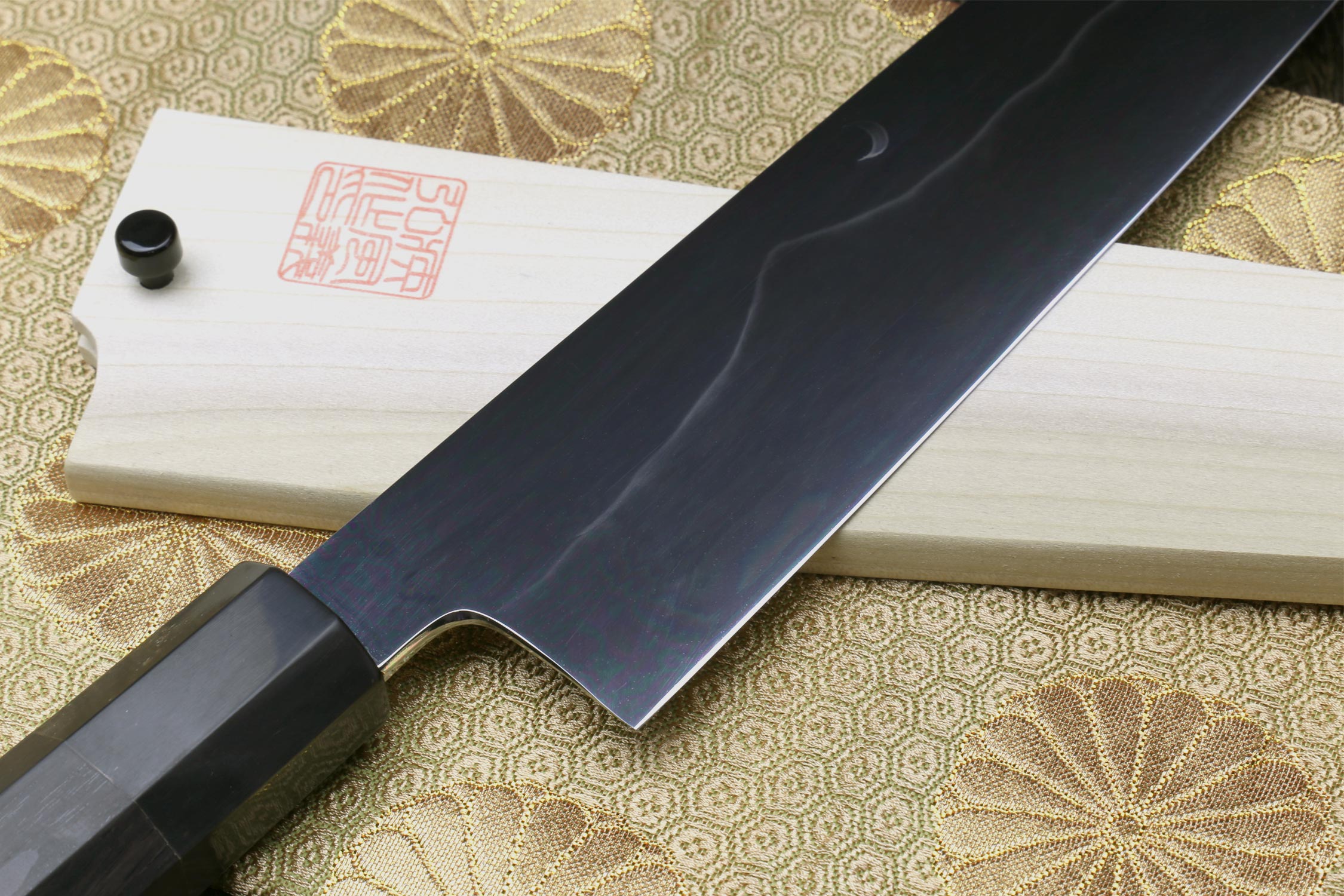 Gyuto chef knife close-up of long dark mirror blade with white handle and red stamp