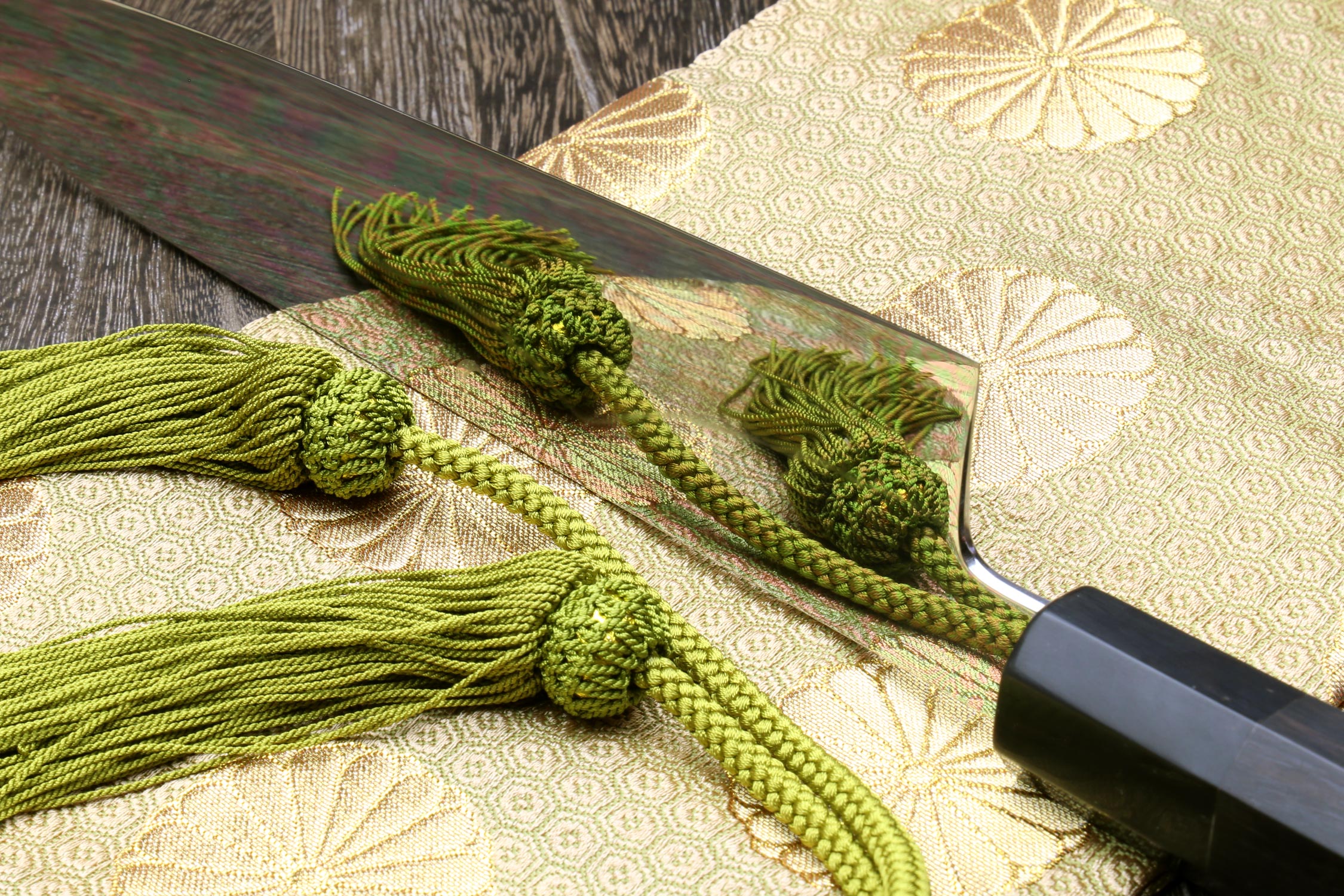 Ebony-handled gyuto chef knife with dark mirror-finished blade and green cord