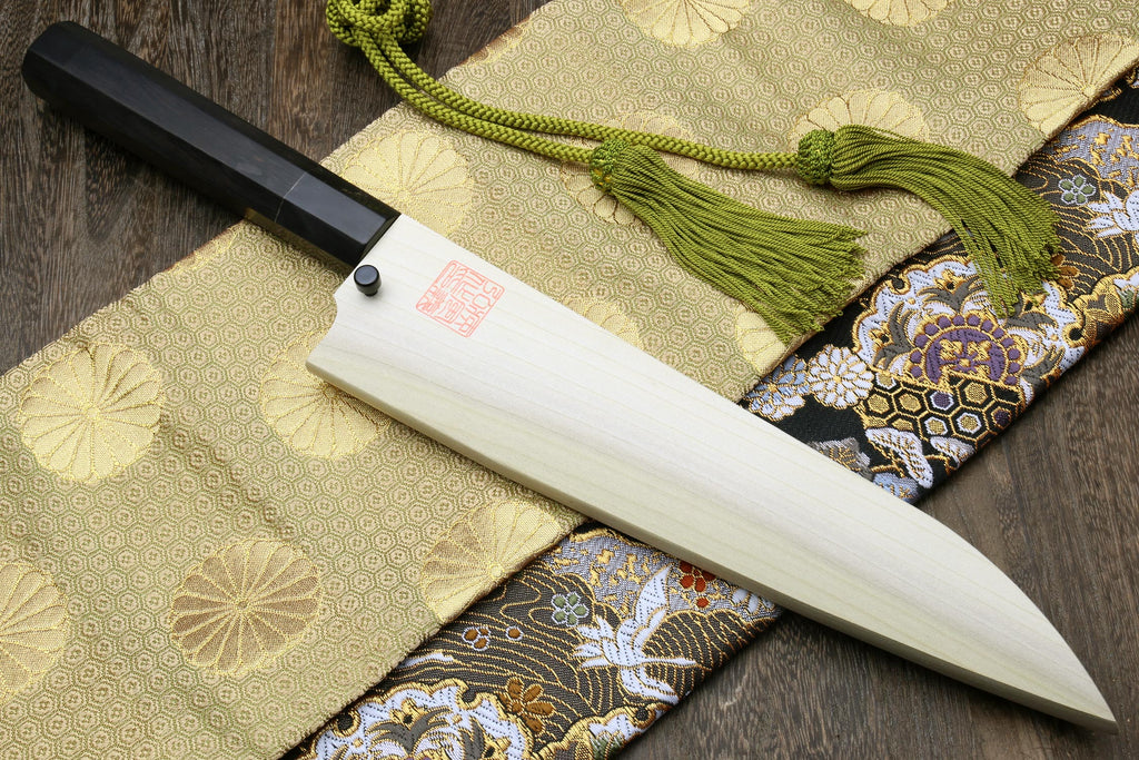 Ebony-handled gyuto chef knife with white handle and green tassel on patterned cloth
