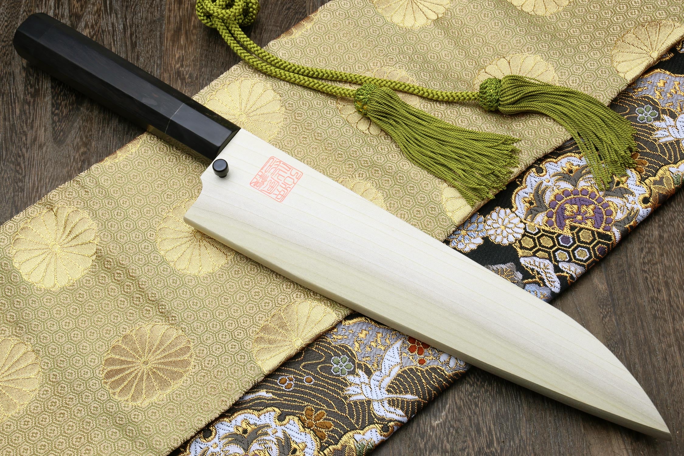 Ebony-handled gyuto chef knife with white handle and green tassel on patterned cloth