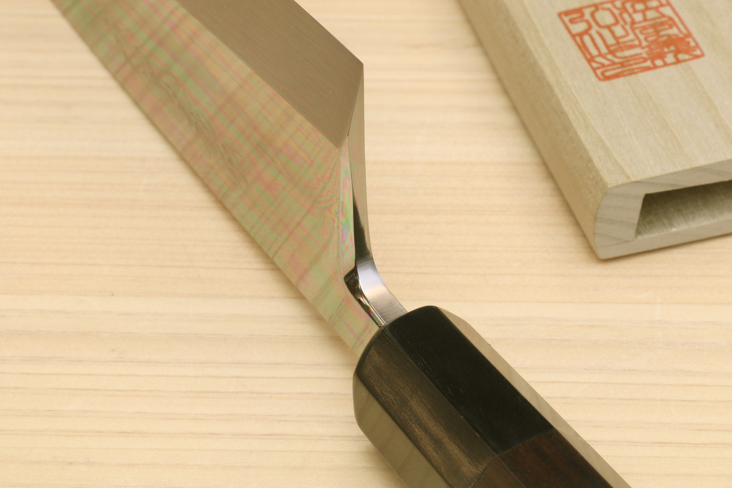 Japanese chef knife with mirror-finished blade edge and black handle, beside wooden saya