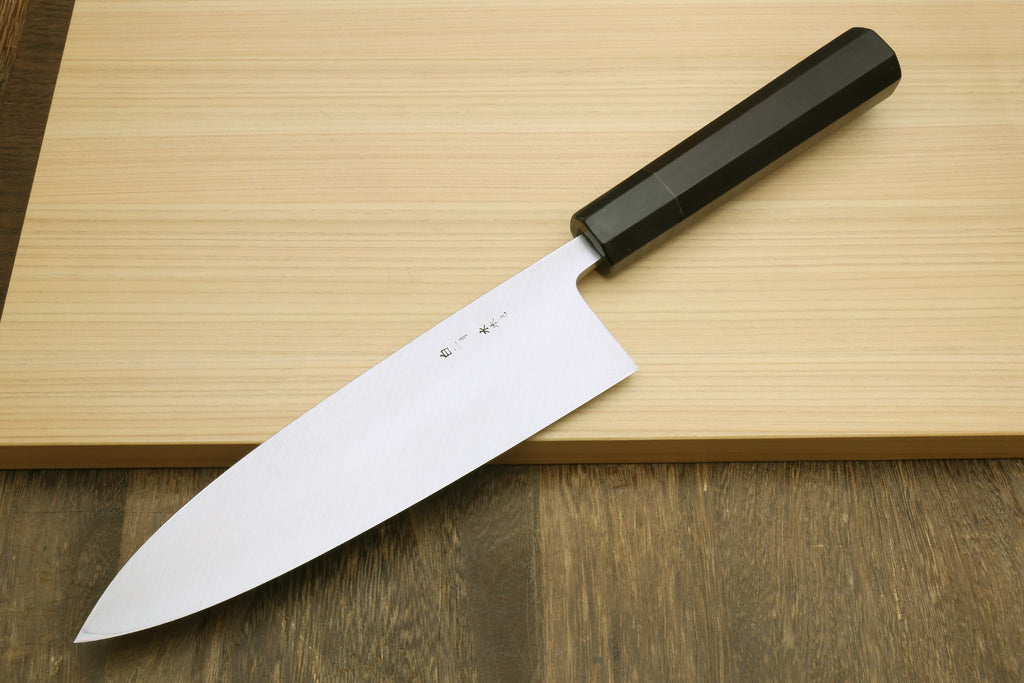 Japanese chef knife with curved silver blade and black handle, on light wooden board