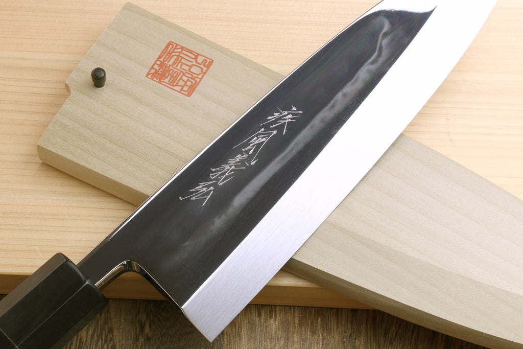 Japanese chef knife blade close-up, dark gray surface with etched markings, in wooden saya