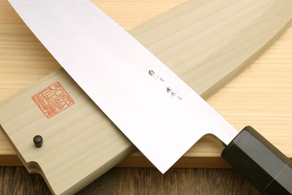 Japanese chef knife with silver blade and etched markings, resting over wooden saya
