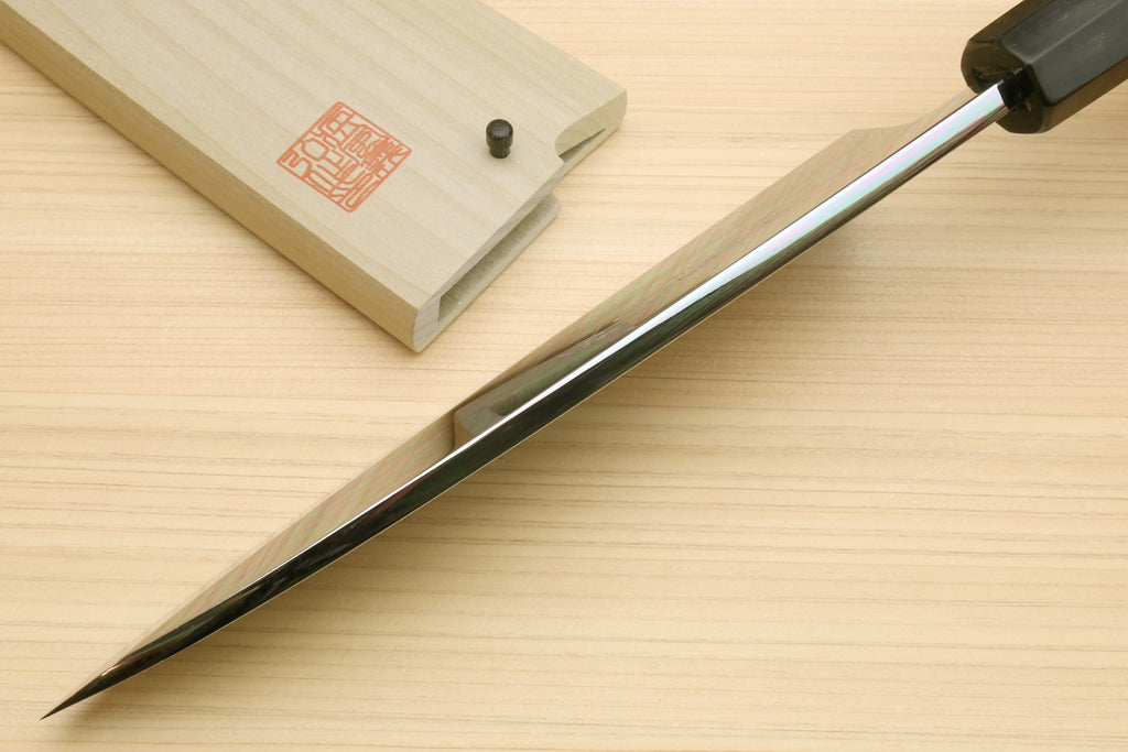 Japanese chef knife with long pointed silver blade and black handle, on light wood