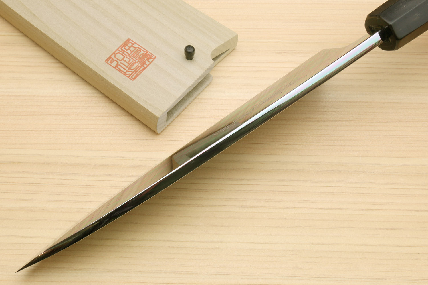 Japanese chef knife with long pointed silver blade and black handle, on light wood