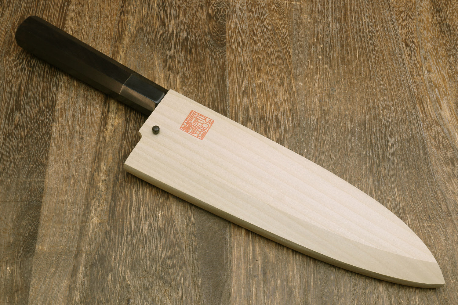 Japanese chef knife with mirror-finished silver blade and black handle, in wooden saya