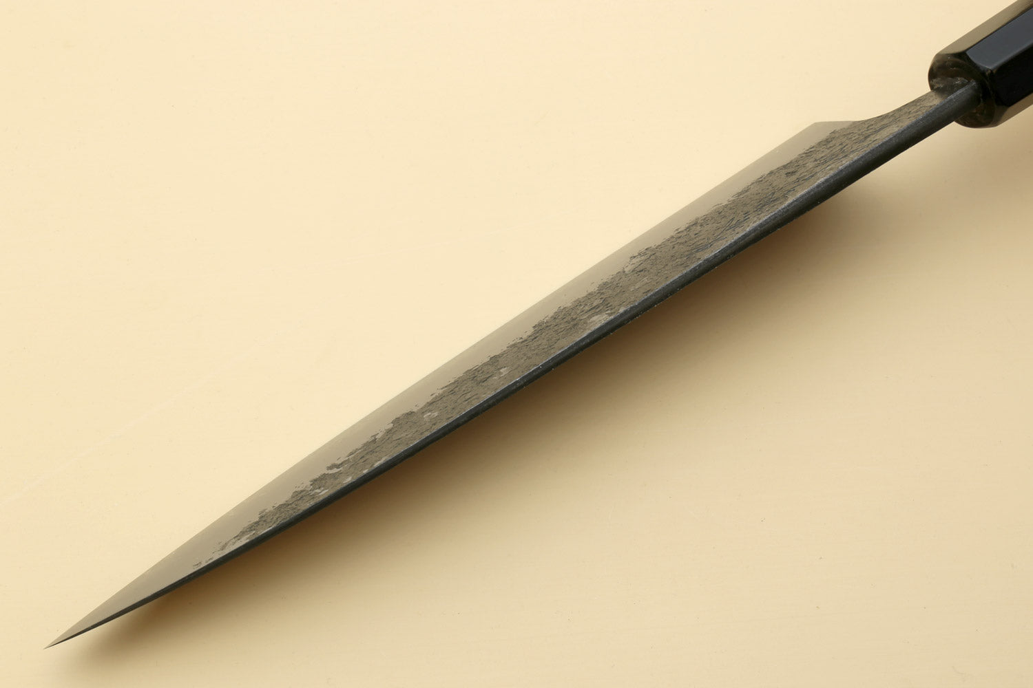 Gyuto knife side view with white steel blade and dark bolster, pointed tip.