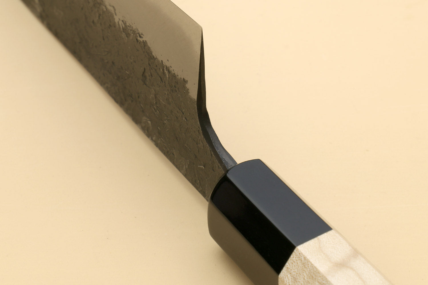 Gyuto knife with curved cutting edge on dark steel blade, black bolster, light handle.