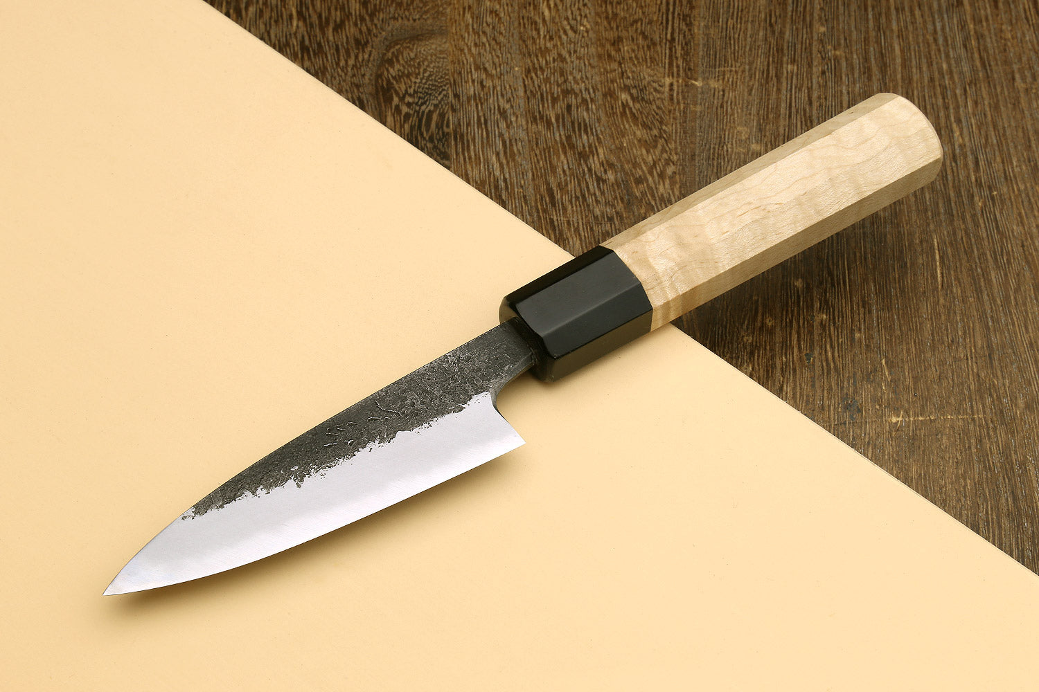 Japanese paring knife with speckled blade, black bolster, and light camphor wood handle