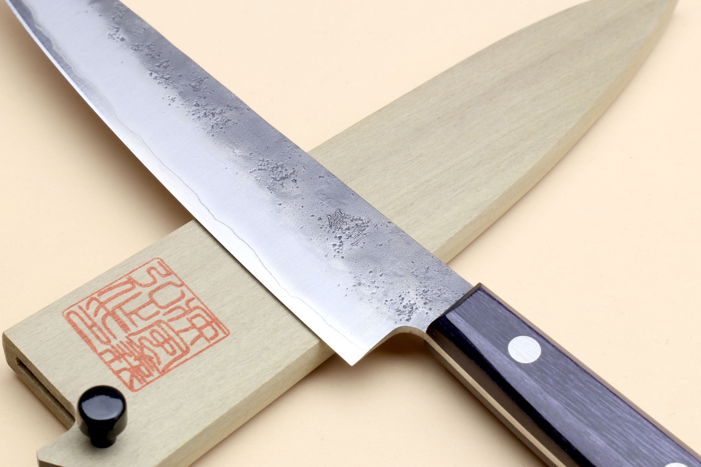Petty utility knife with silver blade and dark handle laid over wooden saya cover