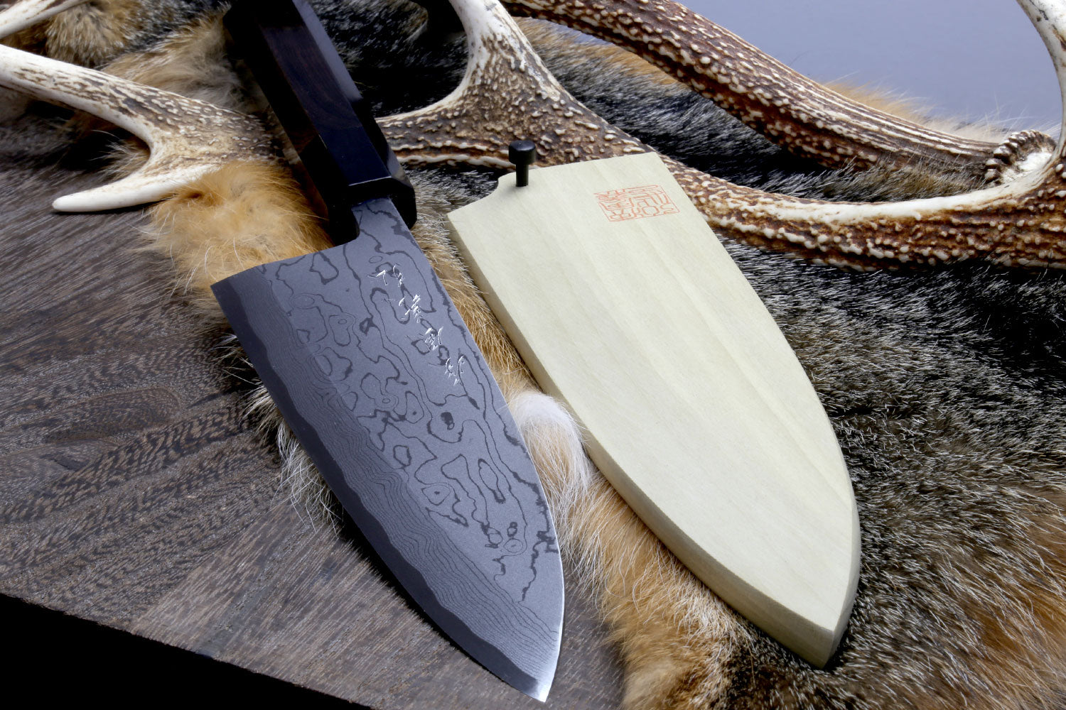 Deba chef knife with patterned steel blade and light handle on fur hide with cord