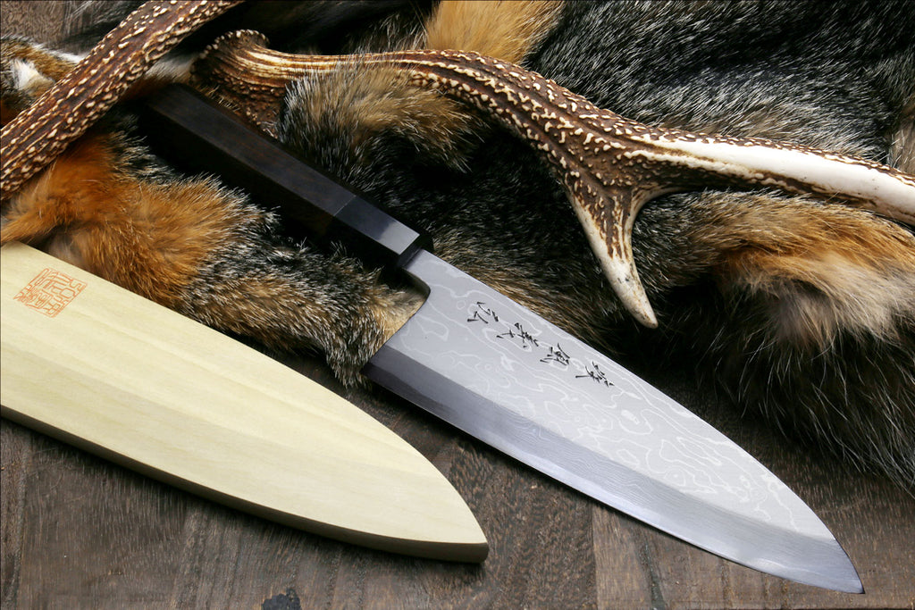 Deba chef knife with patterned blade and light handle beside another knife on fur