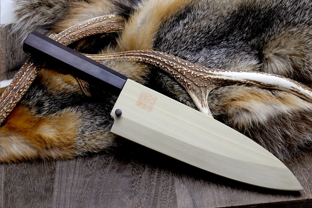 Deba chef knife with patterned steel blade and light wood handle on fur hide
