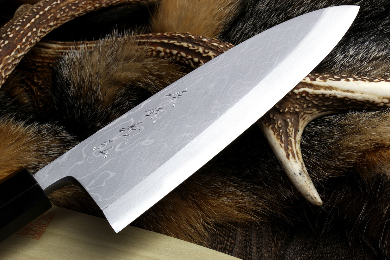 Deba chef knife with textured damascus blade and light wood handle on fur hide