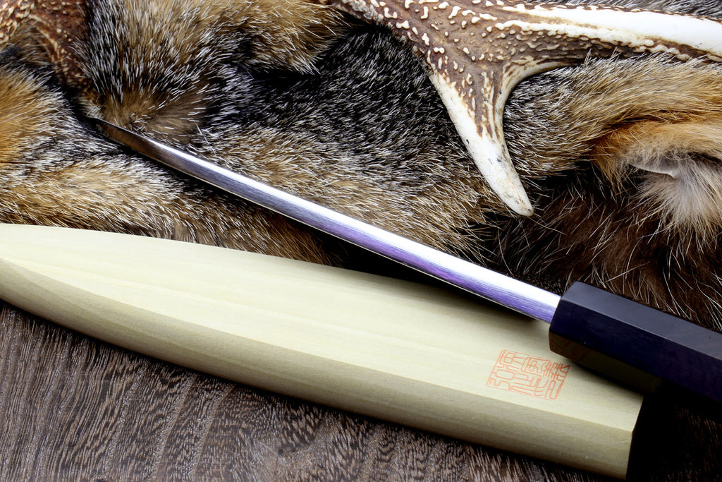 Deba chef knife side view with patterned blade and light wood handle on fur hide
