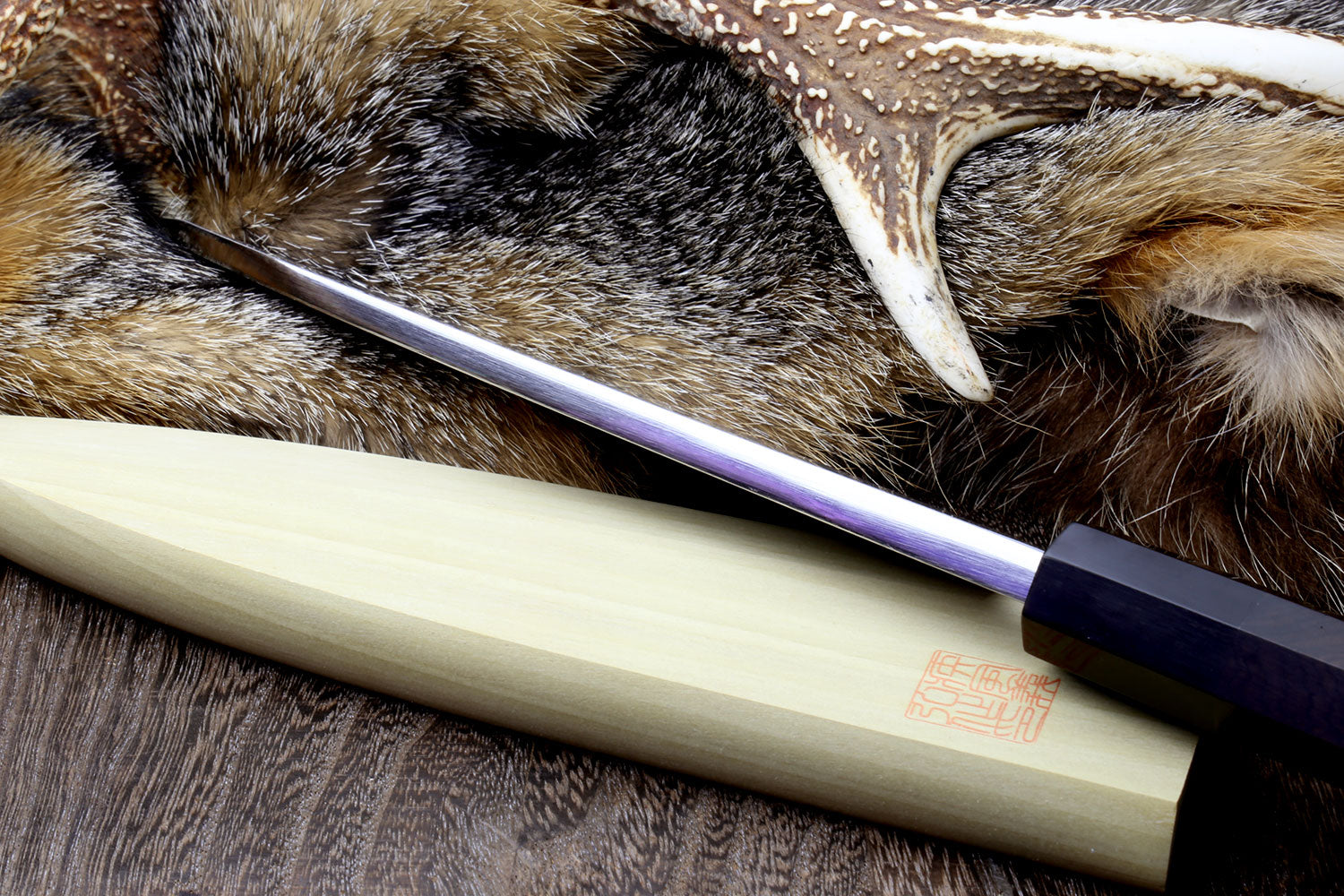 Deba chef knife side view with patterned blade and light wood handle on fur hide