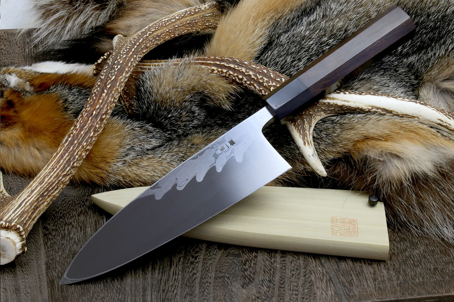 Deba chef knife with patterned blade and light wood handle on fur hide with cord