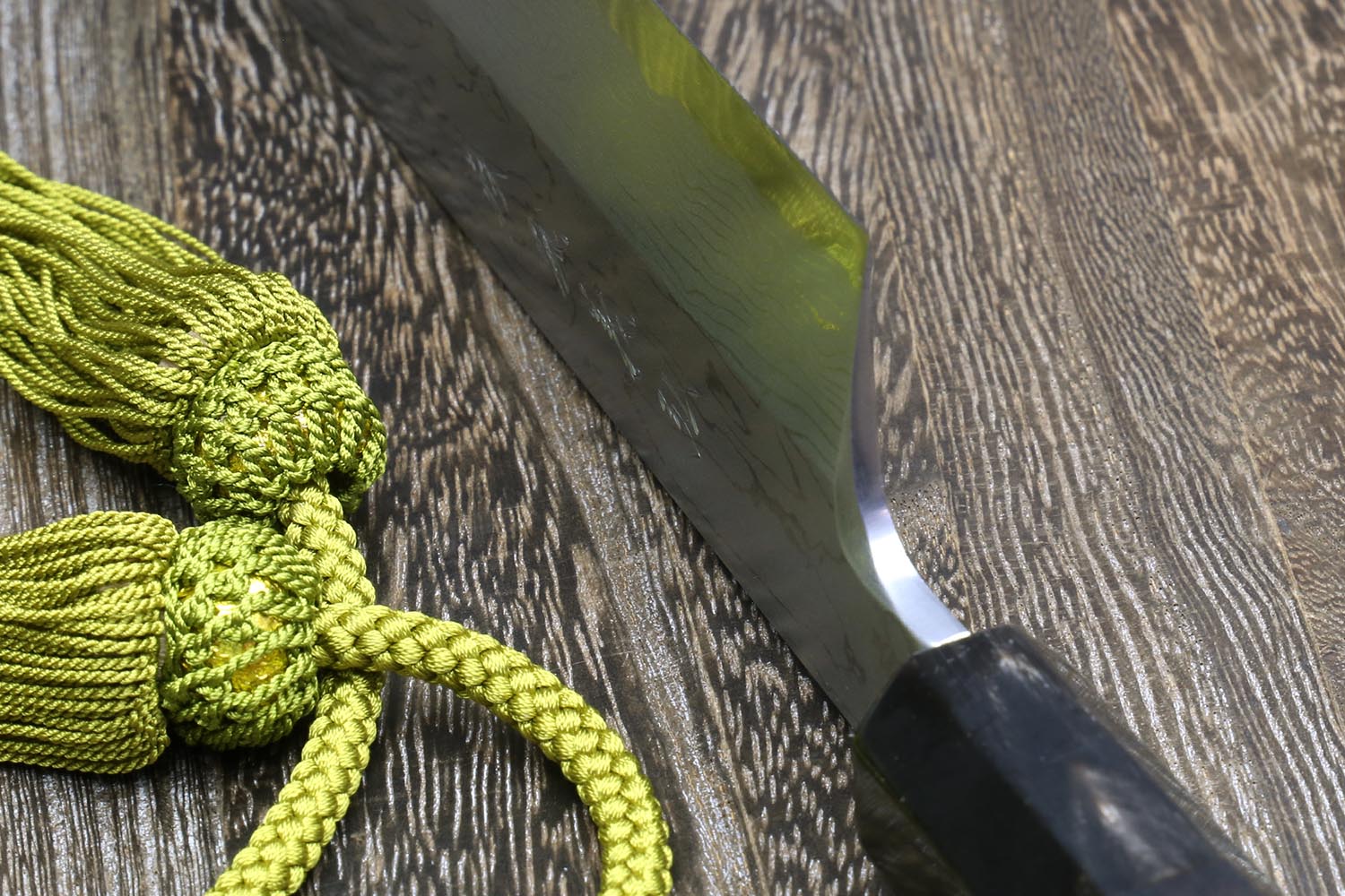 Knife blade edge with reflective bevel and dark bolster; green cord nearby