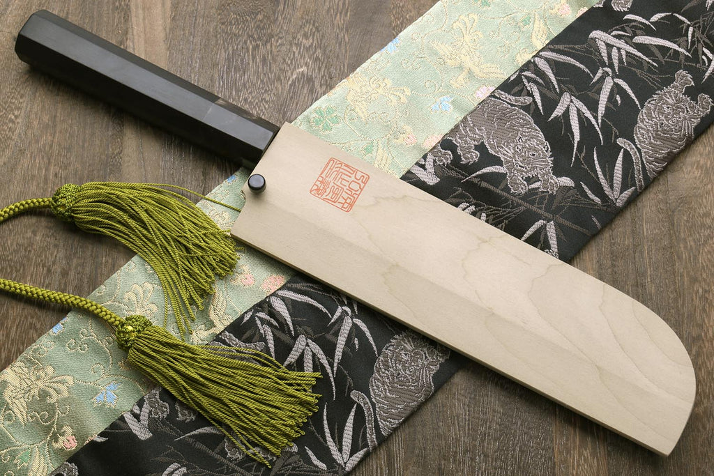 Traditional Japanese vegetable chopping knife with ebony handle, green cord, and sheath