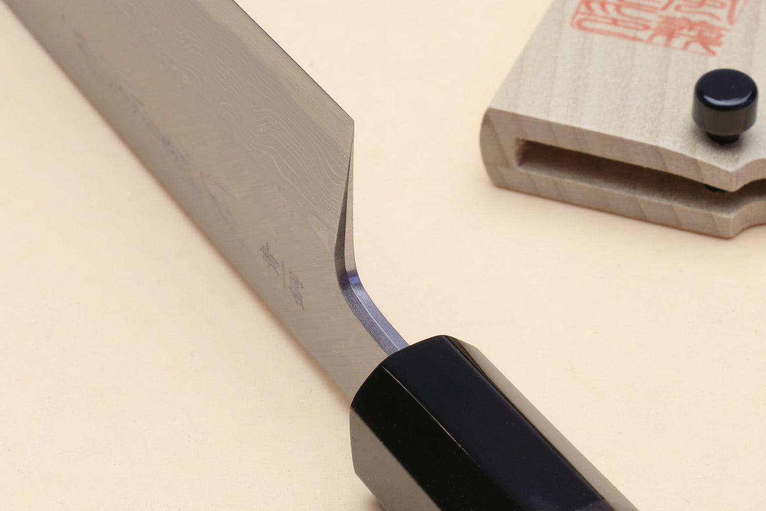 Japanese vegetable knife with curved blade near heel and black handle; wooden saya shown