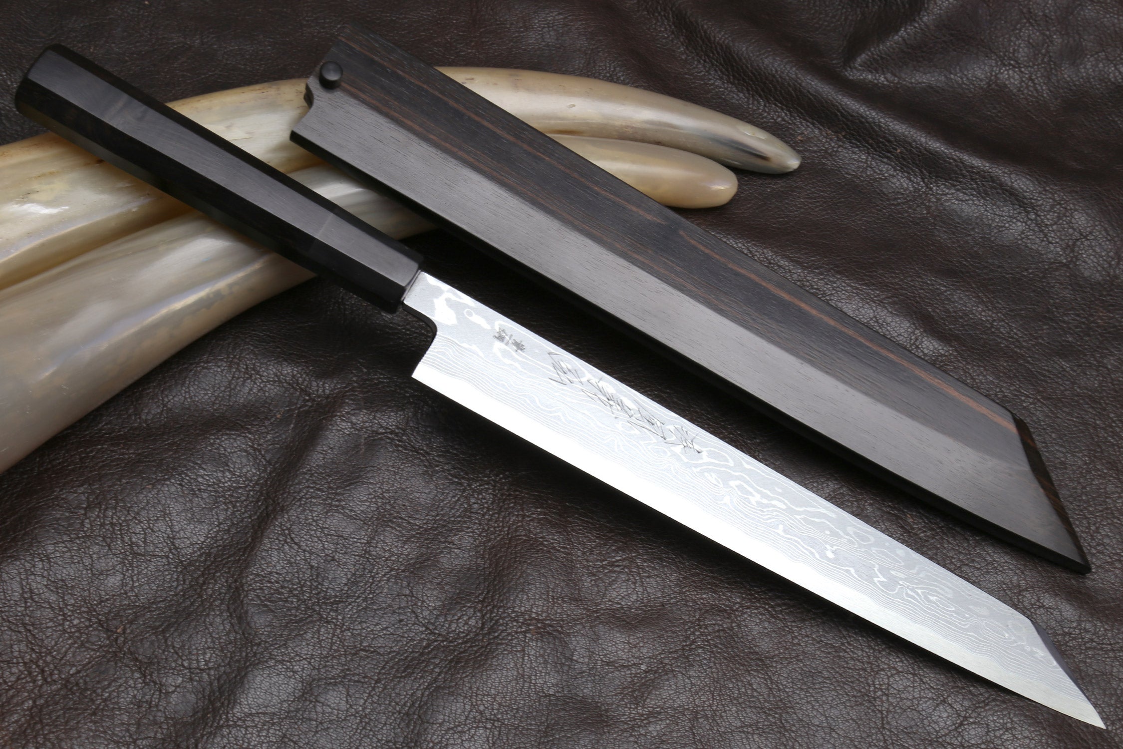Japanese yanagi sushi knife on dark leather, damascus blade with ebony handle