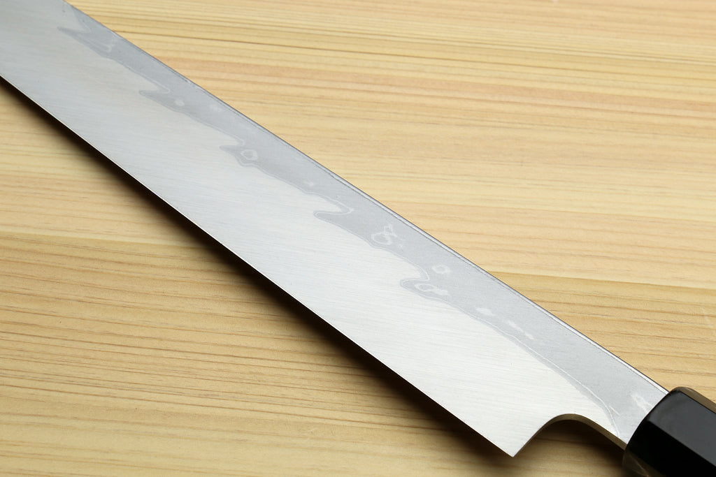 Sashimi knife blade close-up with wavy steel pattern and tapered tip