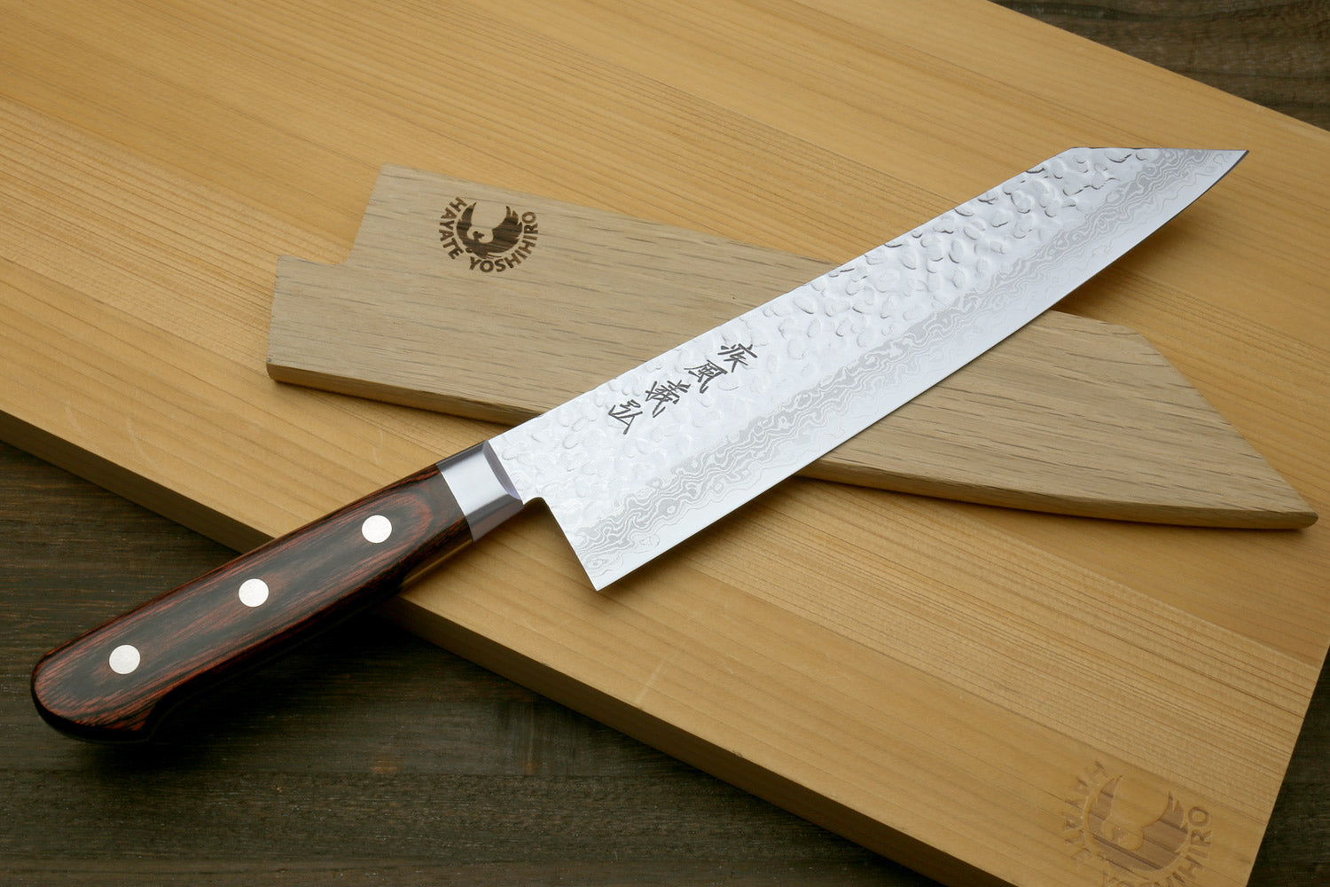 Kiritsuke knife with hammered Damascus blade and dark wooden handle on cutting boards