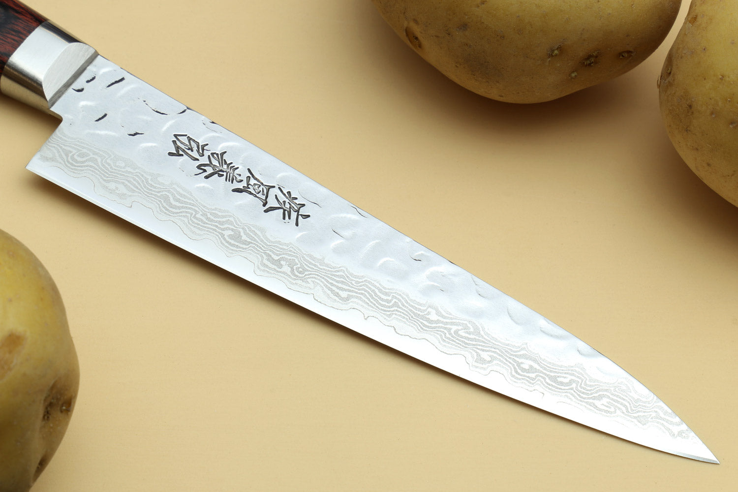 Petty knife blade close-up, hammered Damascus pattern and engraved characters.