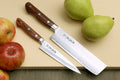 Nakiri and petty knives with dark wood handles and hammered Damascus blades, on board.