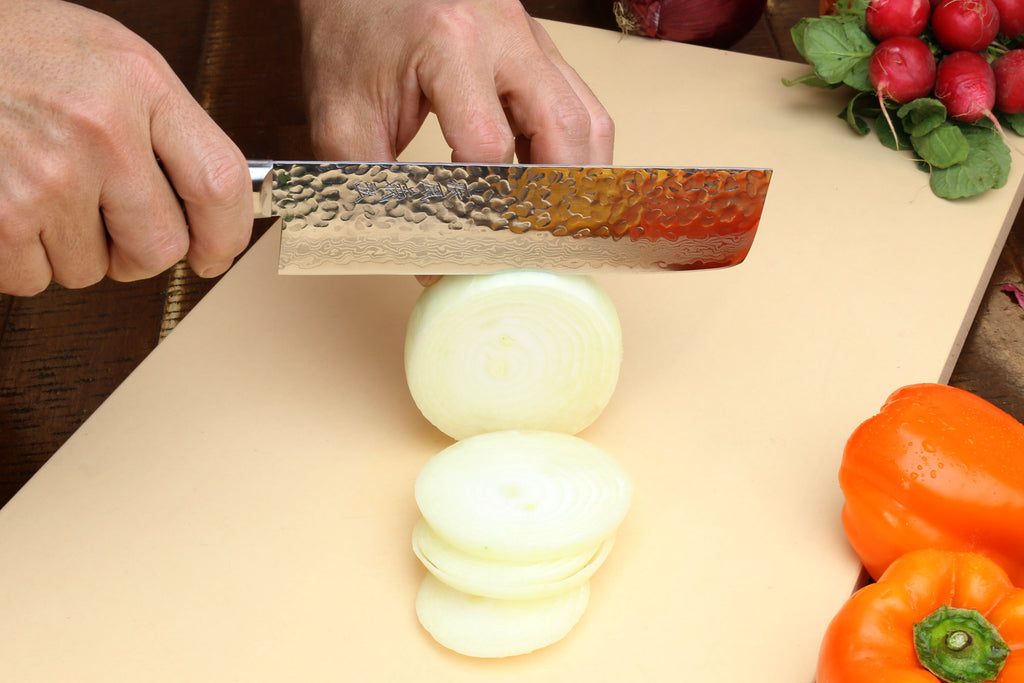 Nakiri vegetable knife slicing onion on a cutting board, dark wood handle visible