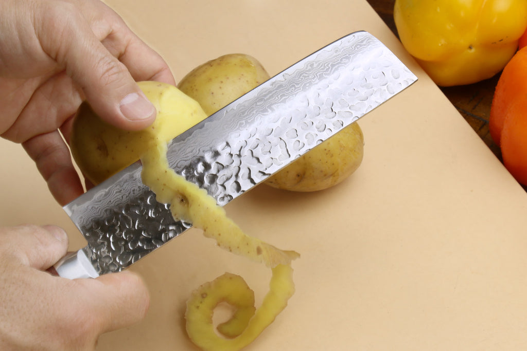 Nakiri vegetable knife cutting a yellow potato, hammered blade and dark wood handle visible