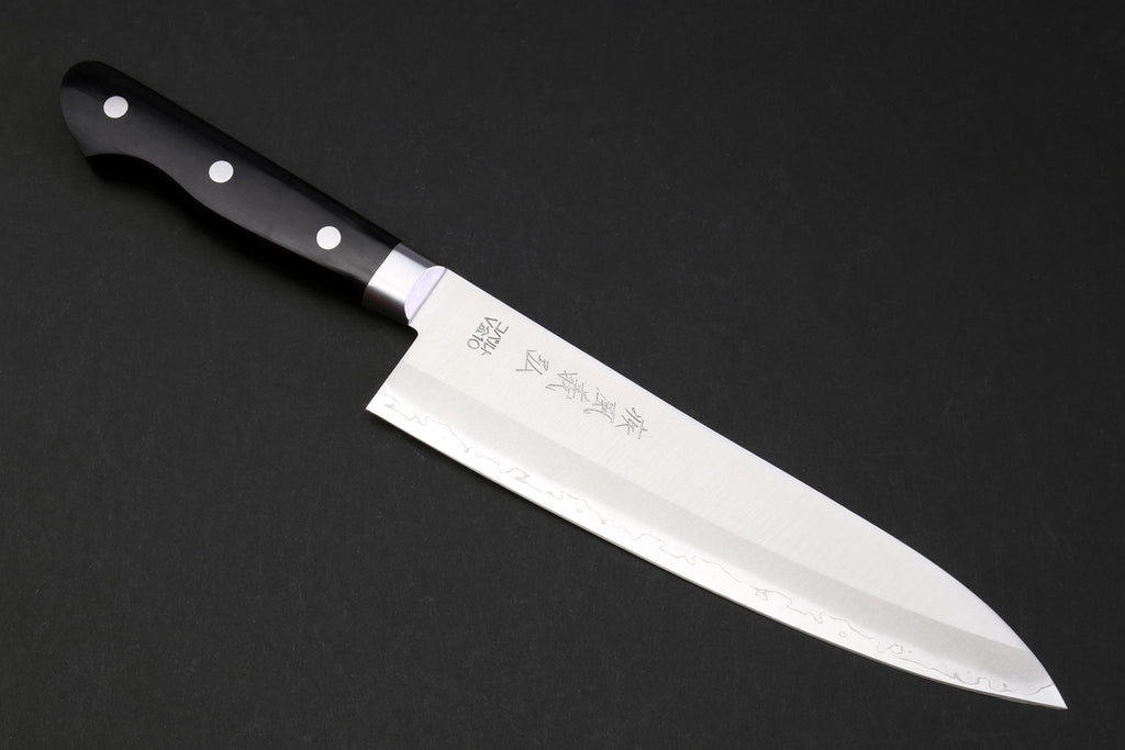 Gyuto chef knife with black handle, silver rivets, and white etched blade.